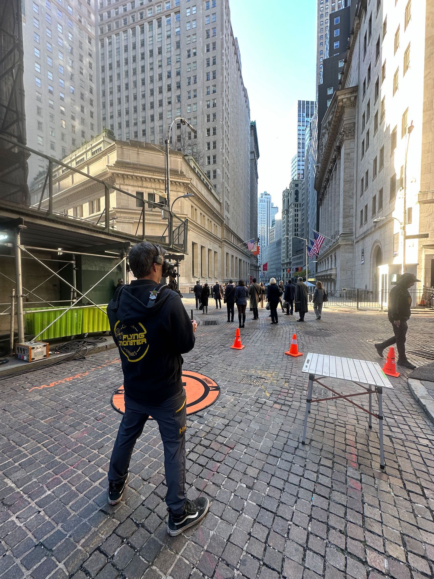 a man standing on at wall street flying a drone wearing a hoodie that says Flying Monster on it