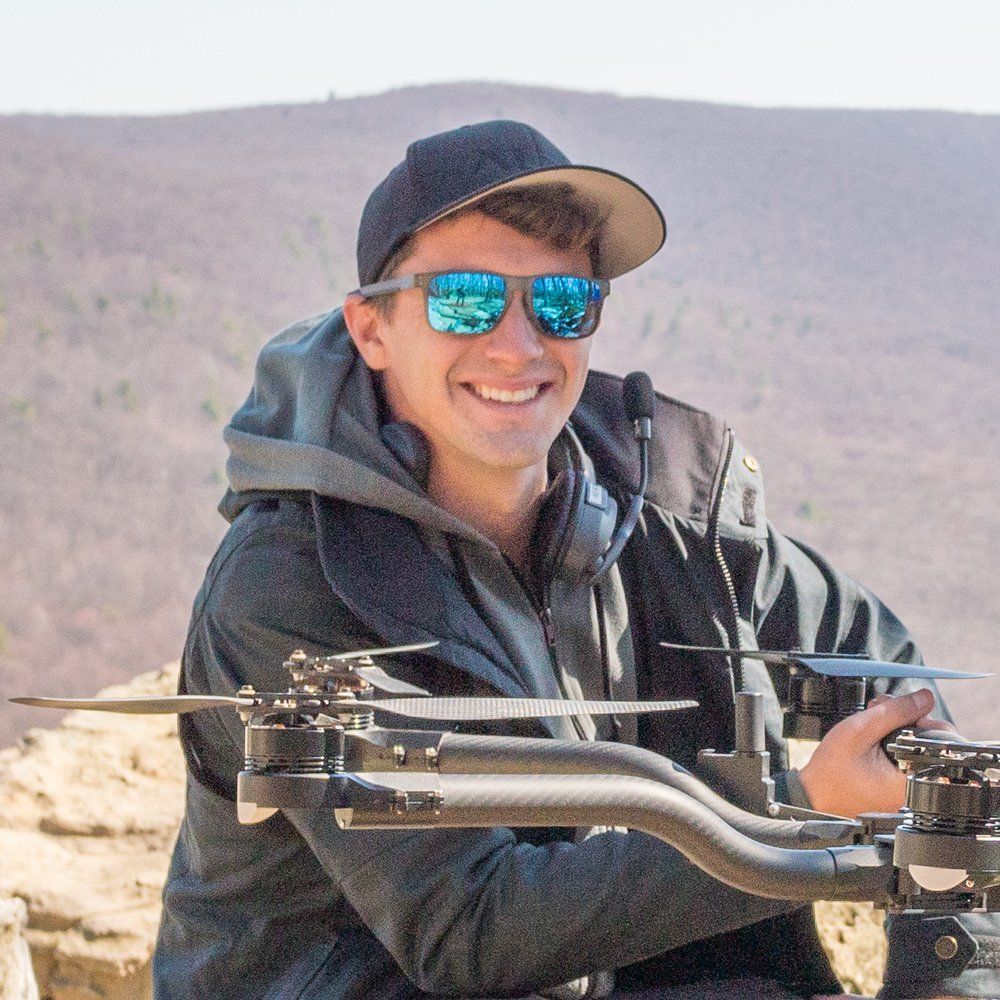 A man wearing sunglasses and a hat is holding a drone.