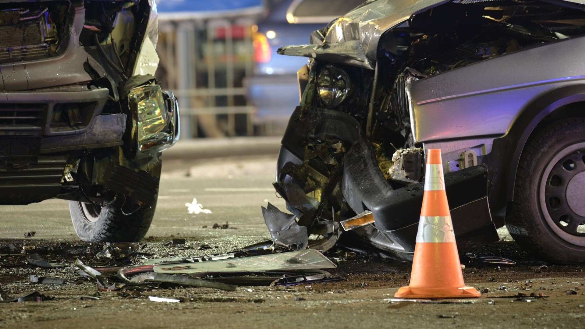 A car accident on a city street with a traffic cone in the foreground.