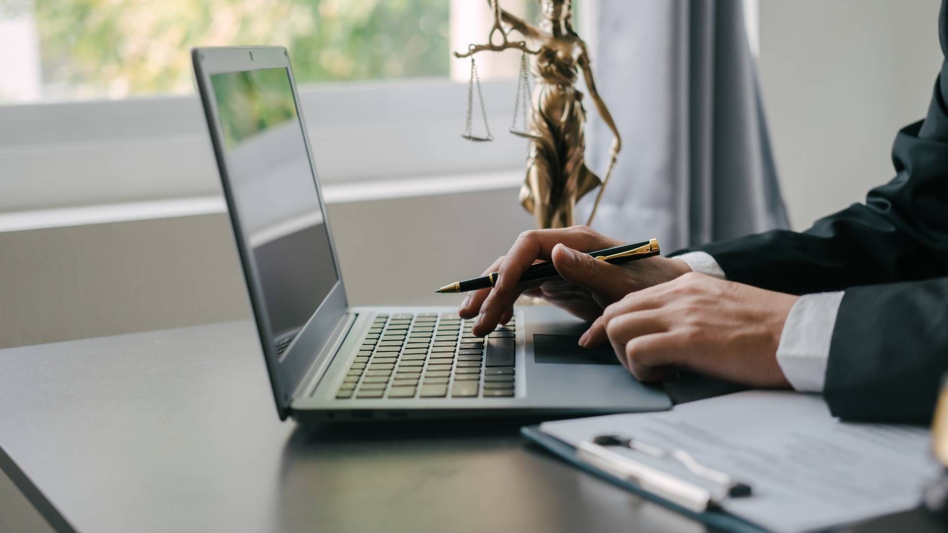 A man is typing on a laptop computer with a statue of justice in the background.