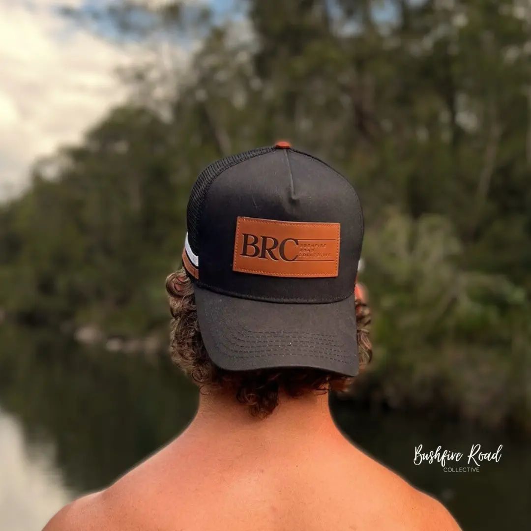Man Wearing A Black Trucker Hat With "Brc" Leather Patch, Standing Near A Body Of Water — Bushfire Road Collective in Mareeba ,QLD