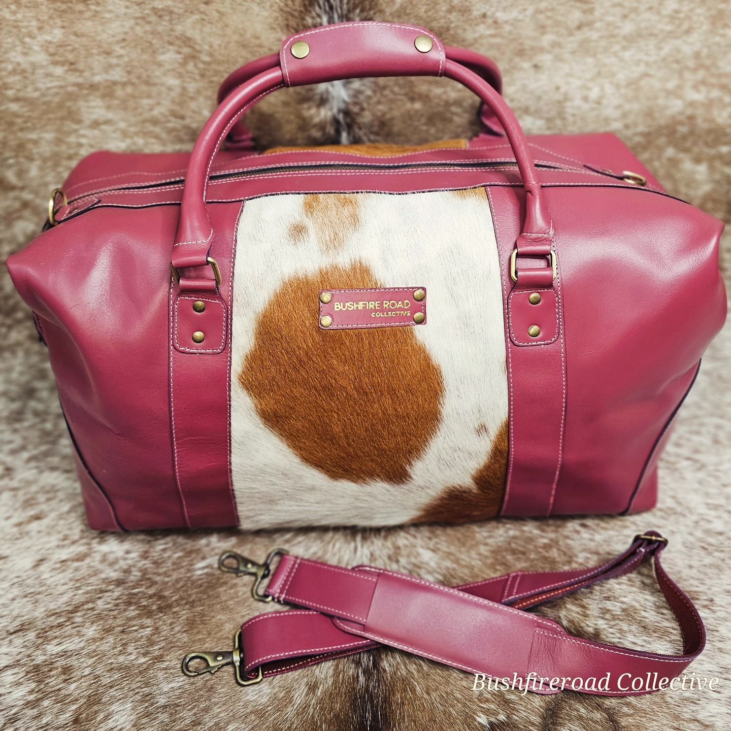 Maroon And Cowhide Travel Bag With Shoulder Strap On A Cowhide Surface — Bushfire Road Collective in Mareeba ,QLD