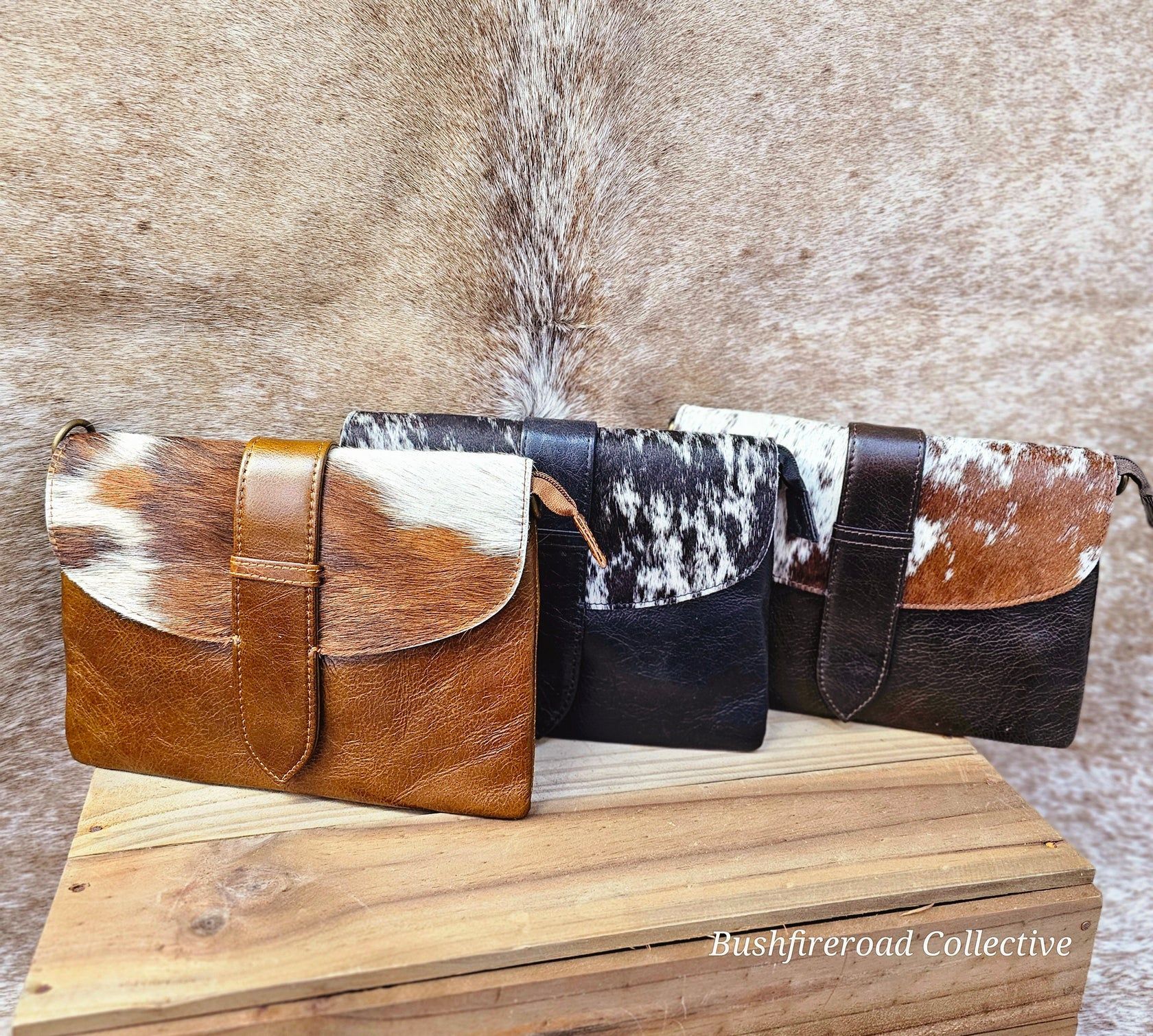 Four Cowhide Leather Clutches, Each With A Different Hair Pattern, Resting On A Wooden Surface — Bushfire Road Collective in Mareeba ,QLD