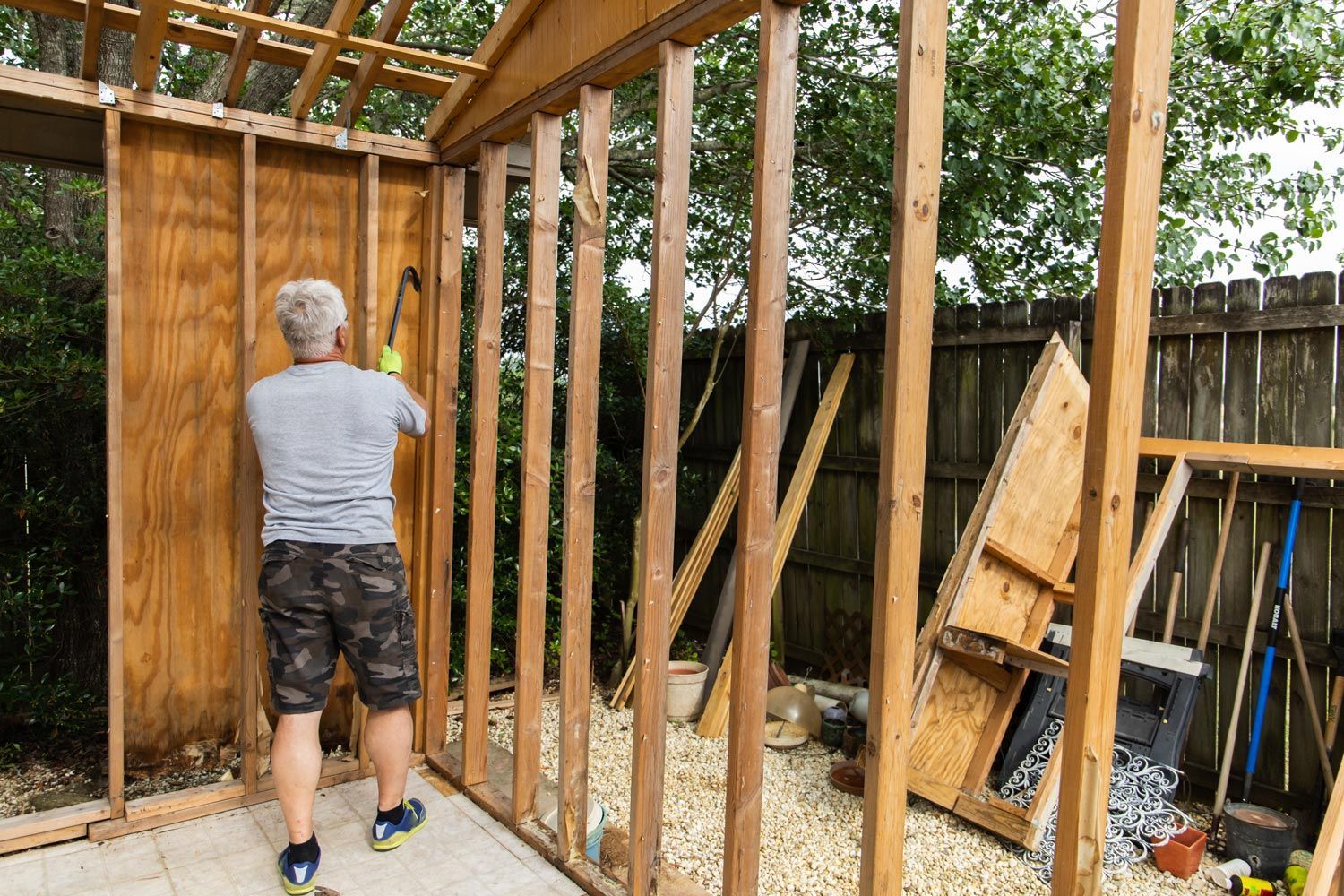 Person framing a wooden shed wall outdoors with exposed studs and tools nearby