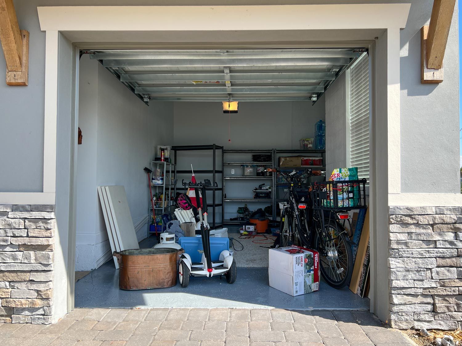 Open garage with shelves, bins, bikes, and a child’s scooter inside.