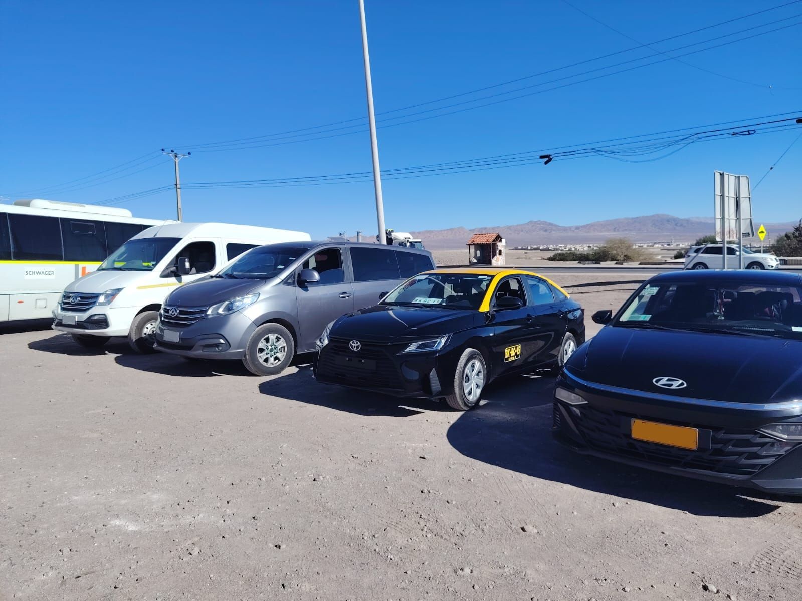 Una hilera de vehículos estacionados, entre los que se incluyen una furgoneta blanca, una minivan gris y dos coches negros