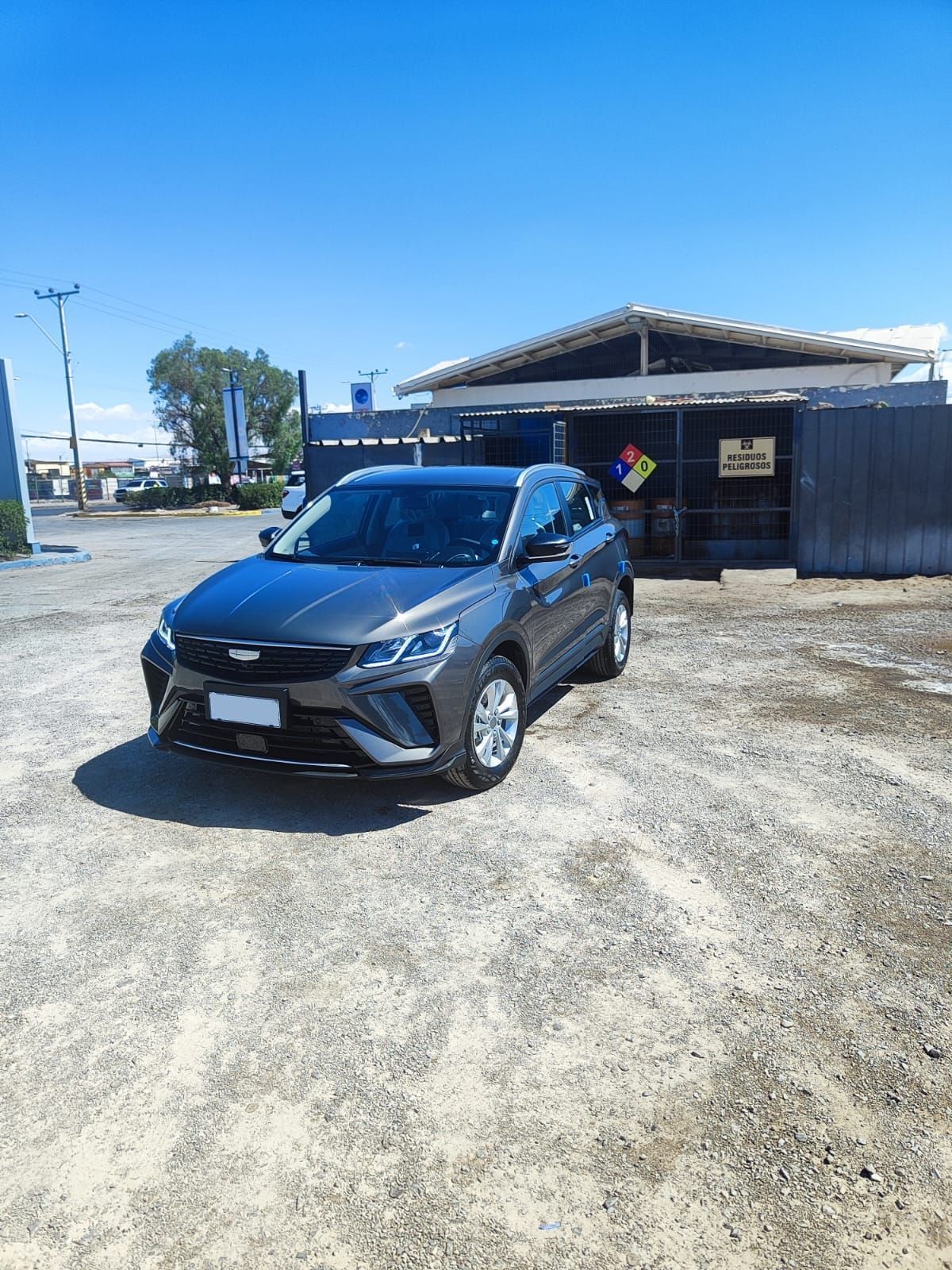 Un SUV gris oscuro estacionado en un terreno de grava frente a un cobertizo bajo un cielo azul despejado.