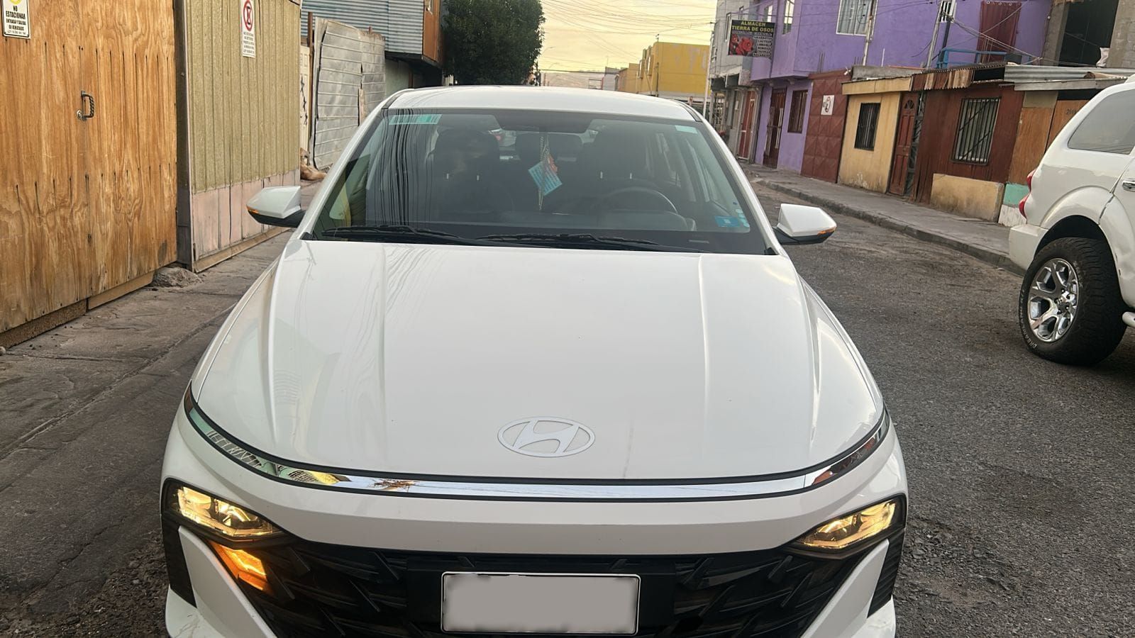 Un sedán Hyundai blanco estacionado en una calle estrecha durante el día, visto desde el frente.