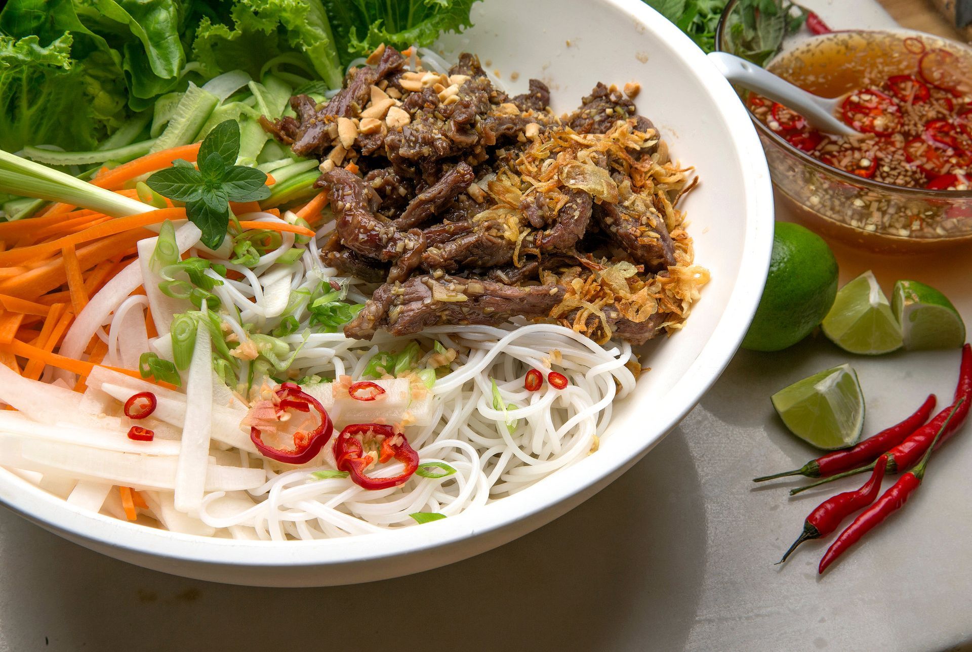 Bowl of Vietnamese noodle salad with beef, vegetables, and chili sauce.