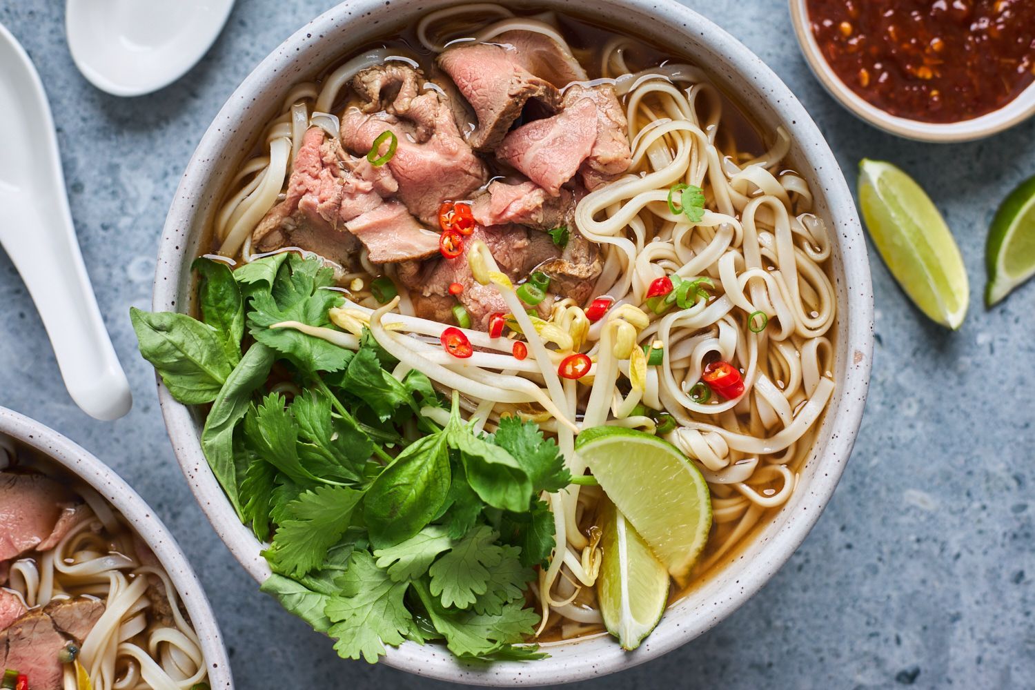 Bowl of pho with noodles, beef, herbs, bean sprouts, and lime slices.