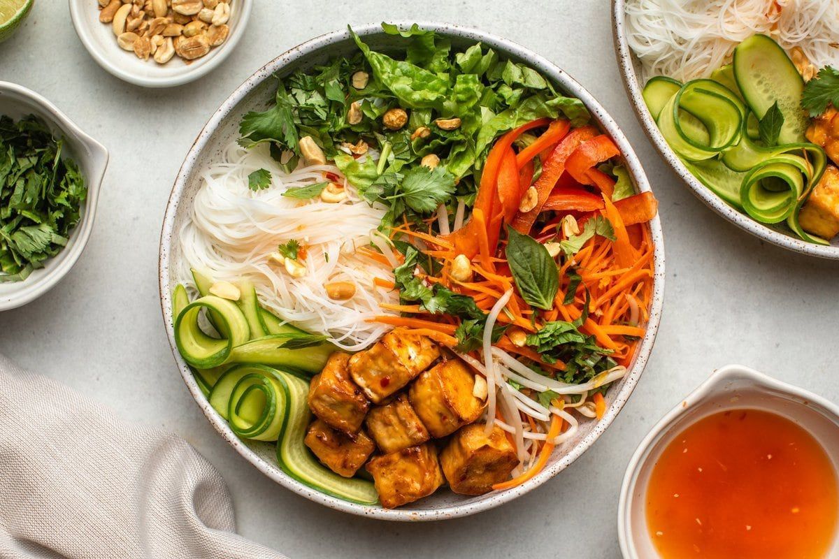 Bowl of Vietnamese food: vermicelli noodles, tofu, vegetables, peanuts, sauce.