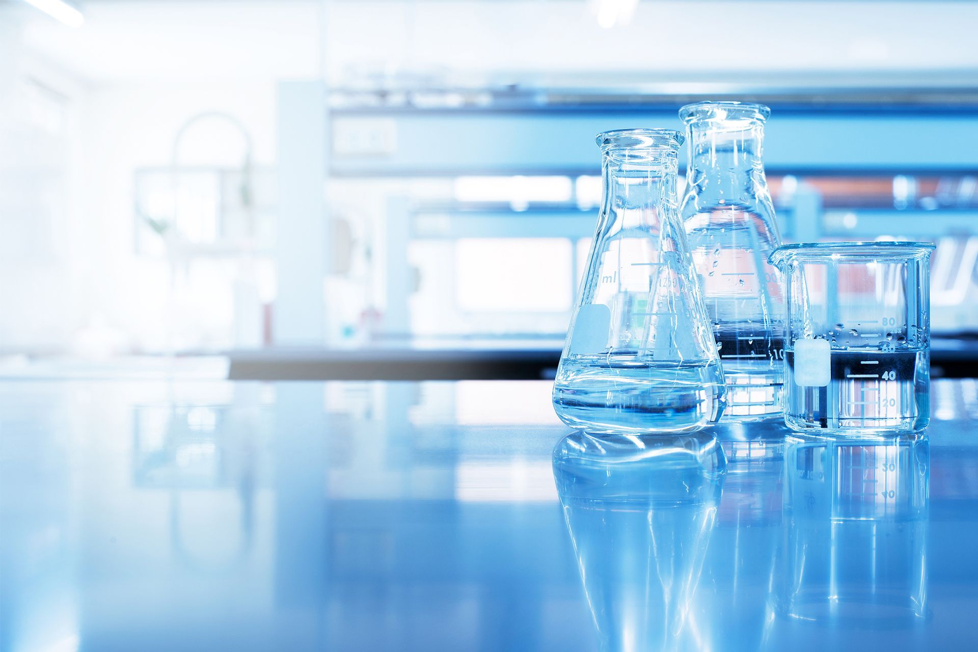 Blue laboratory beakers and flasks on a reflective lab bench, with a blurred science background
