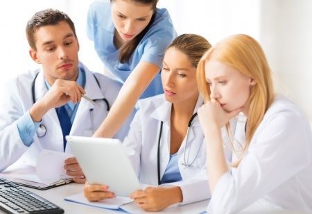 Medical team gathered around a laptop in a clinical setting, discussing a document with focused expressions