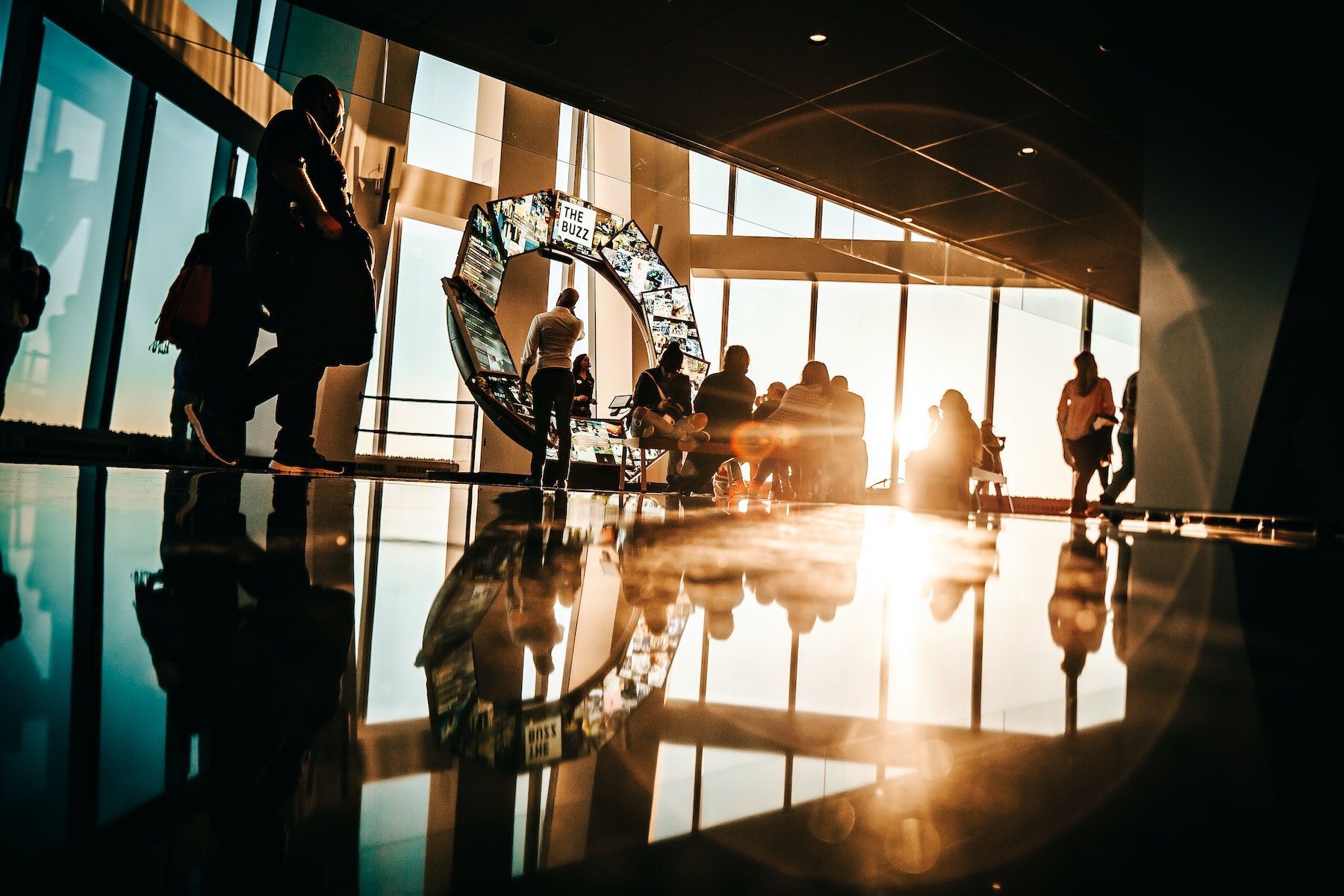 Silhouetted people in a modern lobby at sunset, with bright reflections on the polished floor.