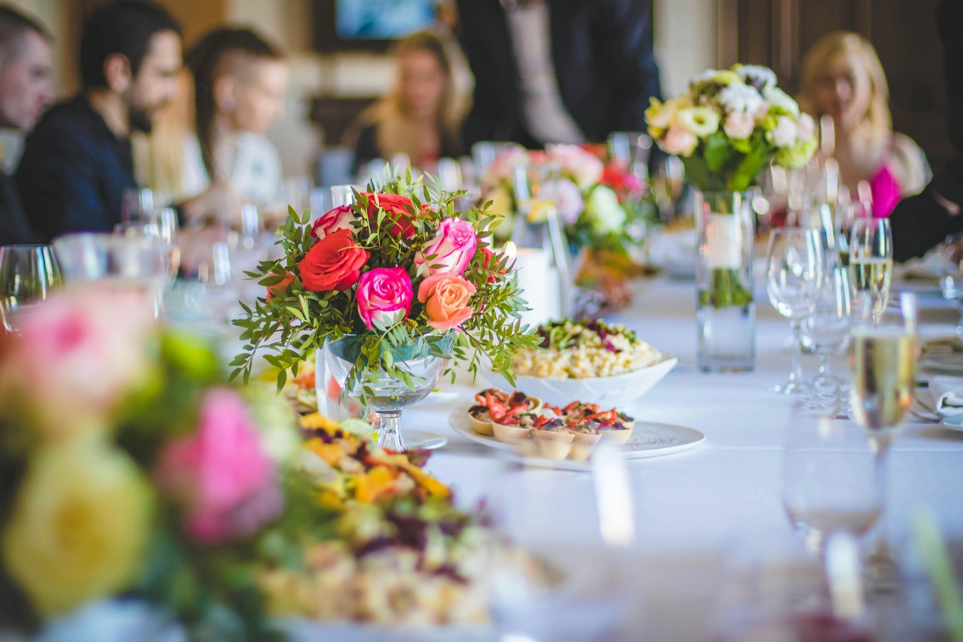 Elegant banquet table with colorful floral centerpieces, plates of food, and guests blurred in the background