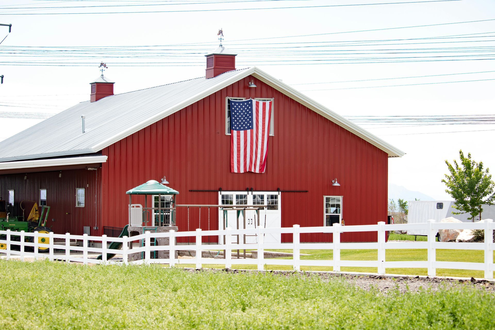 Red barn with an American flag and white fence in a grassy field