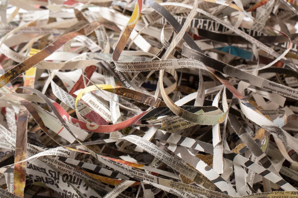Shredded strips of paper, primarily newsprint, piled in a heap.