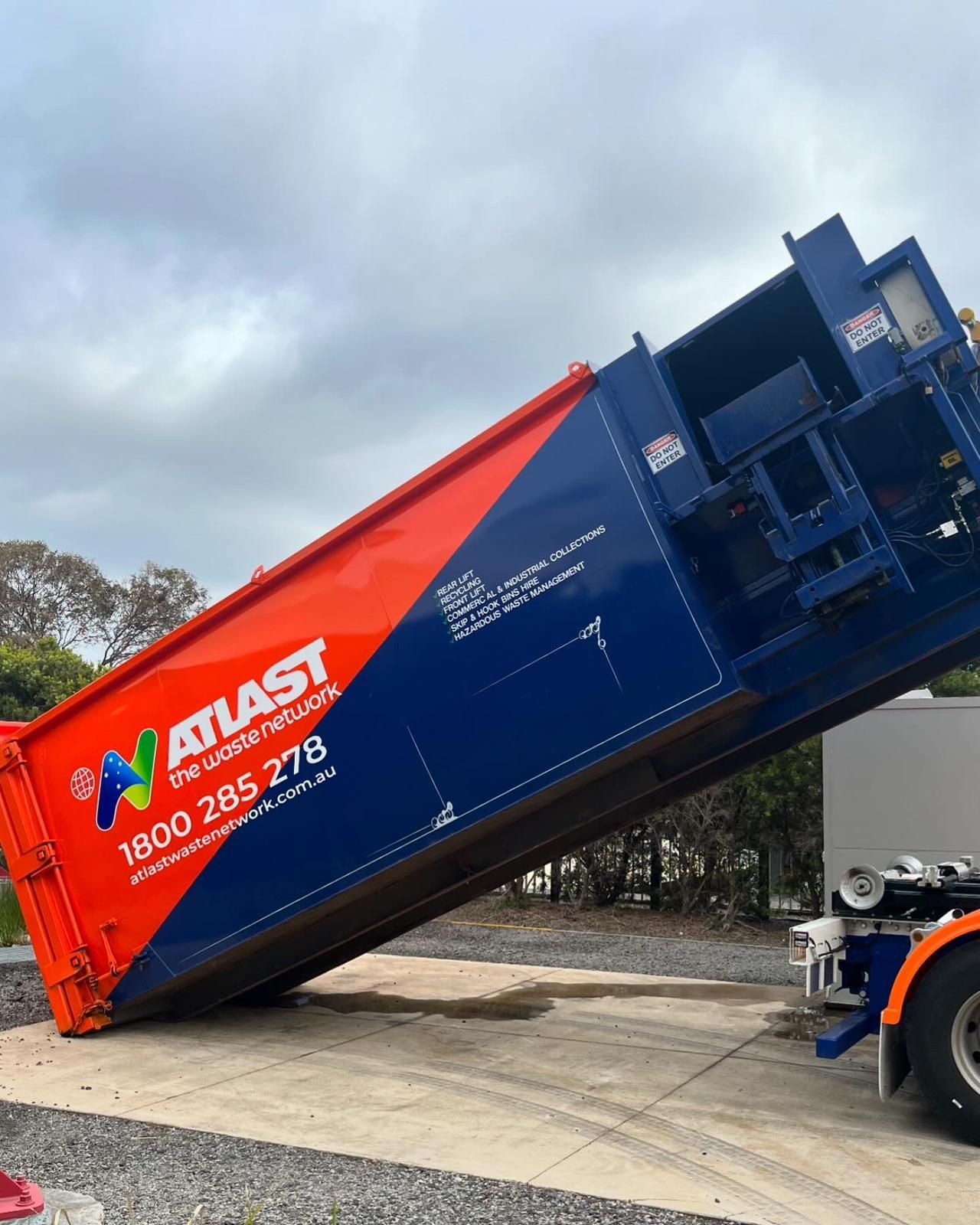 Orange and blue Atlast recycling truck, raised bed, unloading waste.