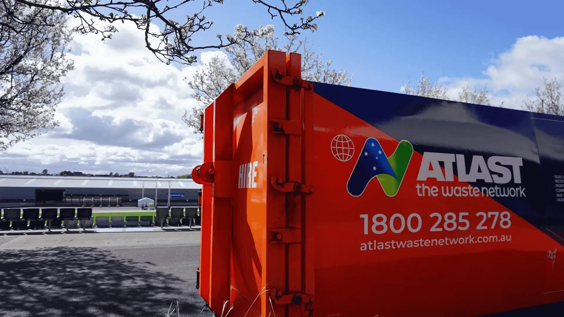 Orange Atlas waste container against a bright sky, with a building in the background.