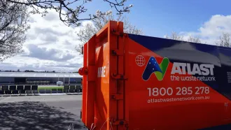 Orange Atlas waste container against a bright sky, with a building in the background.