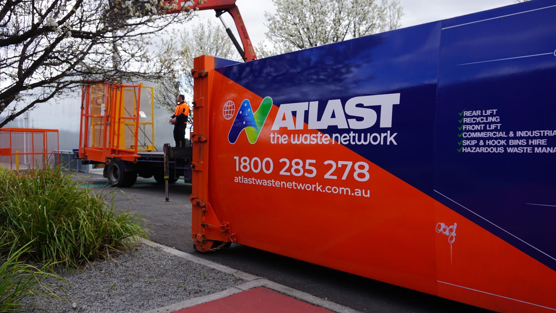 Orange and blue Atlast waste truck with a worker, collecting waste containers.