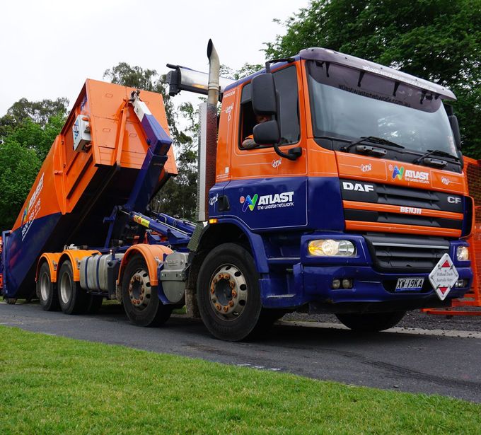 Orange and blue dump truck on a road, cargo bed raised.