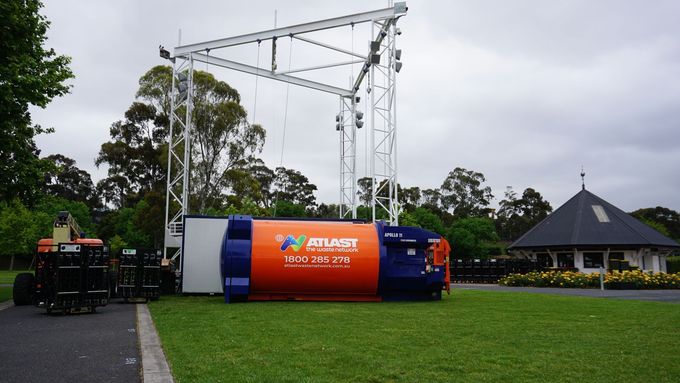 Back of a person wearing an orange vest with the Atlas logo, in a waste recycling facility.
