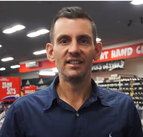 Man in blue shirt smiles in a retail store setting.
