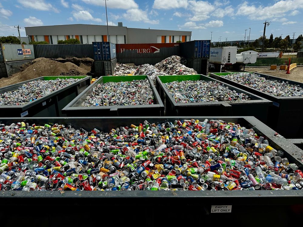 Recycling center with bins full of colorful plastic bottles and containers under a bright sky.