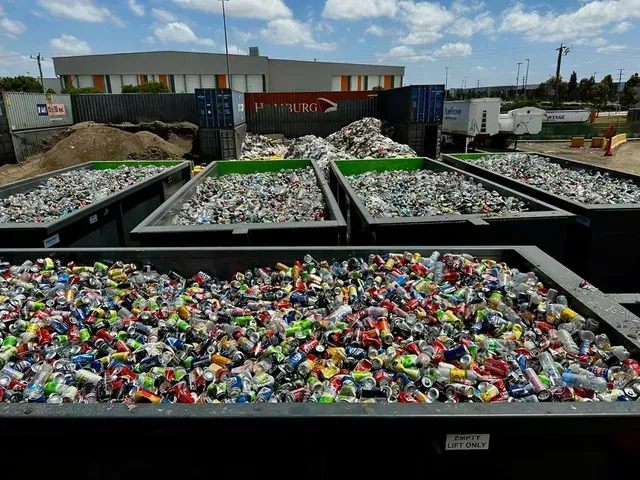 Recycling center with bins full of colorful plastic bottles and containers under a bright sky.