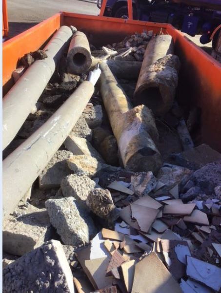 Orange bin filled with broken concrete, tiles, and cylindrical concrete poles.