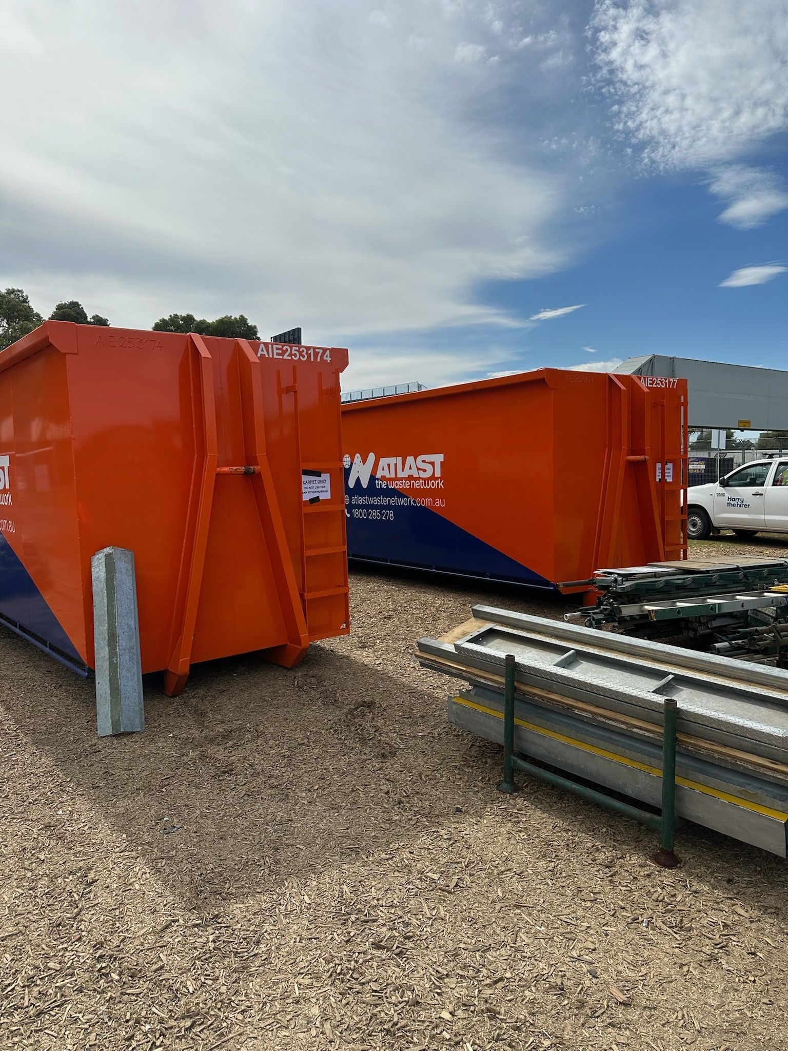 Two orange and blue waste containers on gravel, under a cloudy sky.