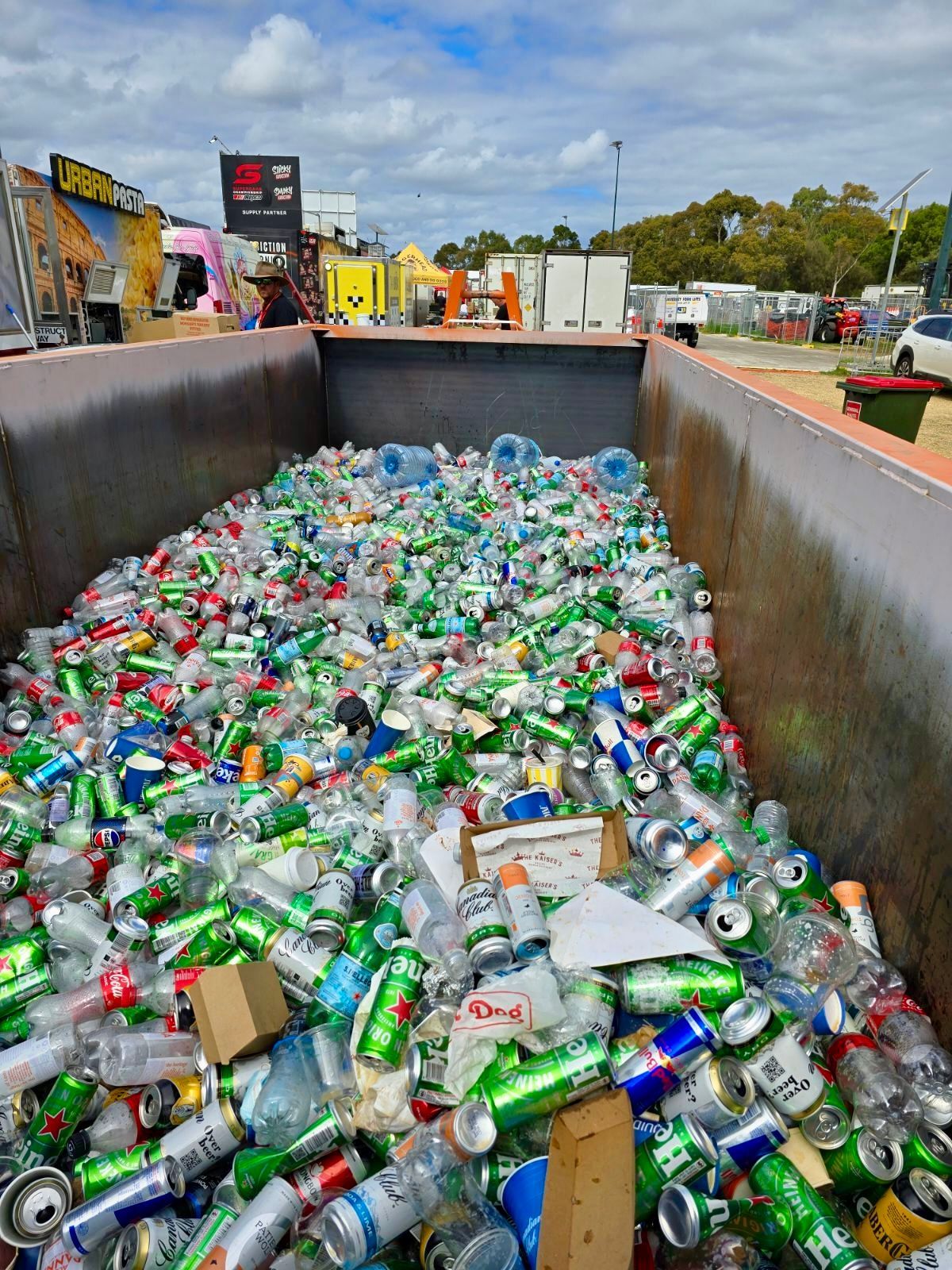 Large bin overflowing with aluminum cans and plastic bottles at a recycling center.