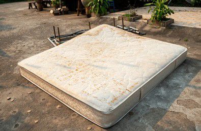 Dirty, stained mattress on a concrete surface outside.