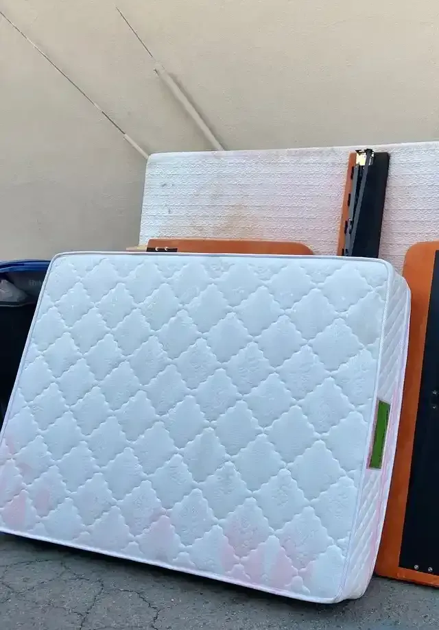 White mattress propped up against more discarded items in an outdoor setting.