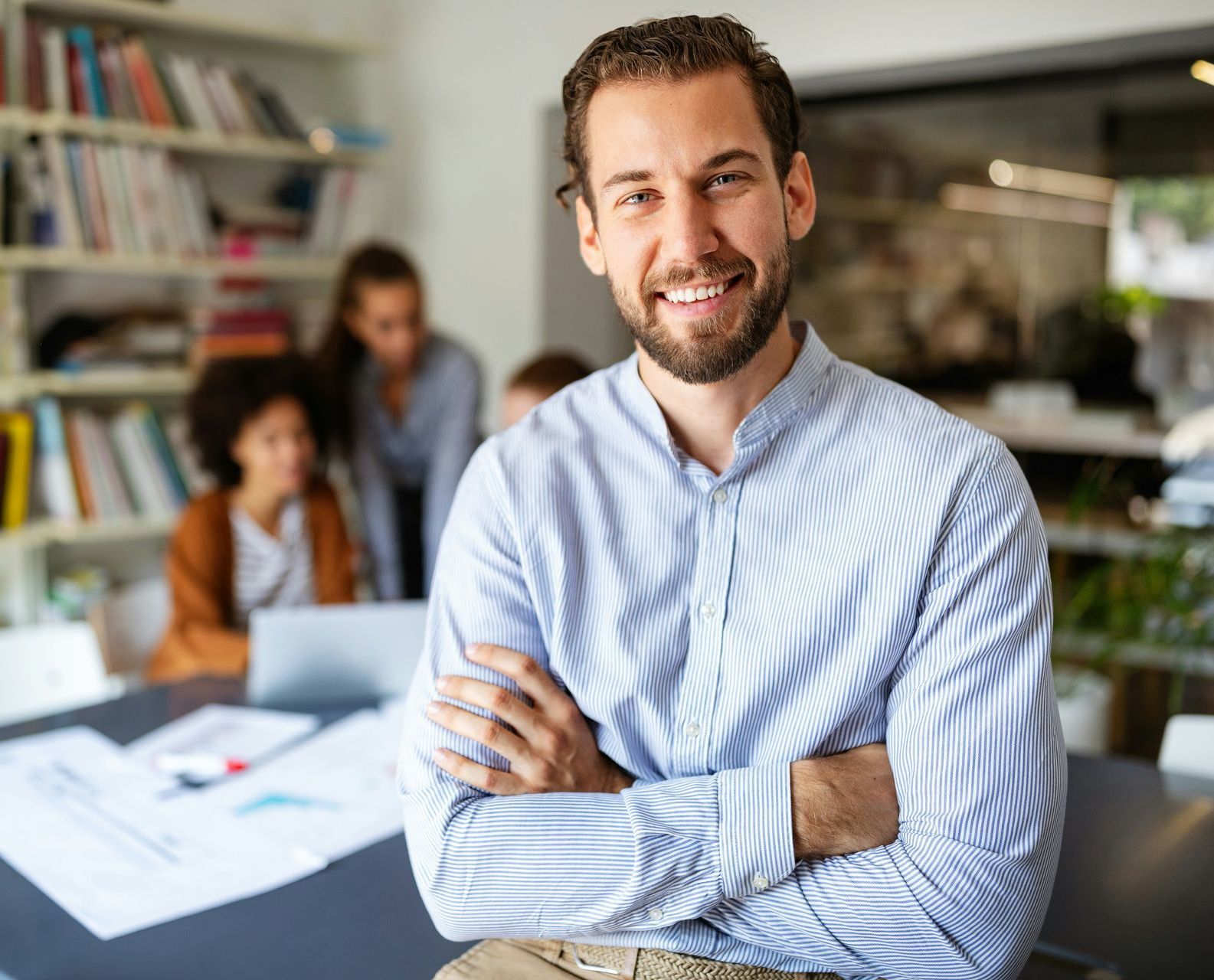 A man is sitting at a table with his arms crossed and smiling.