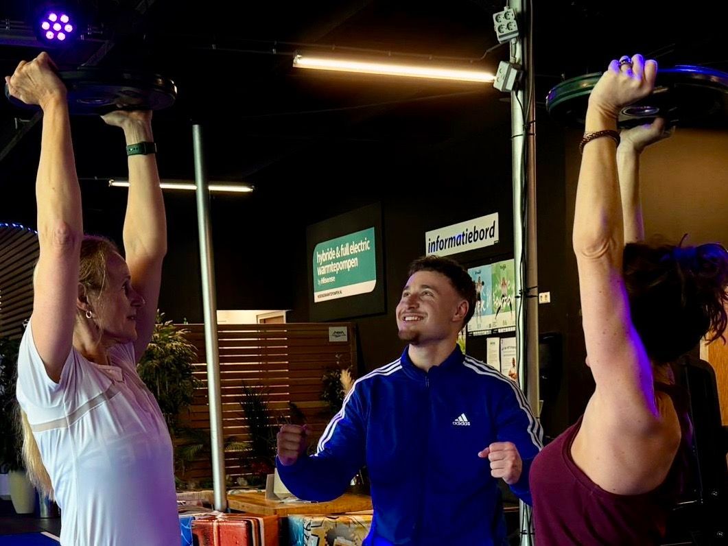 Mensen trainen in een sportschool. Een vrouw doet gewichtheffen boven het hoofd. 