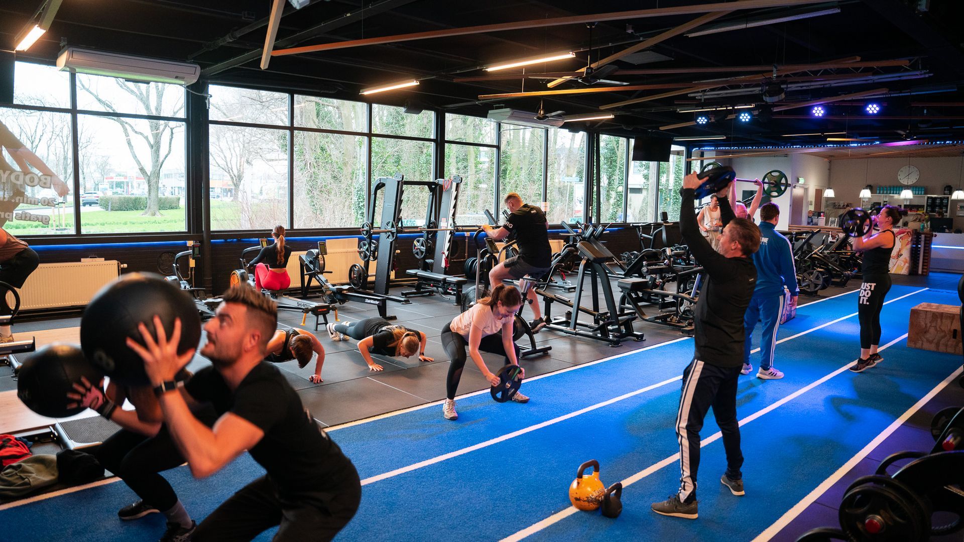 Mensen trainen in een sportschool. Blauwe lijnen op de vloer, fitnessapparatuur en grote ramen.