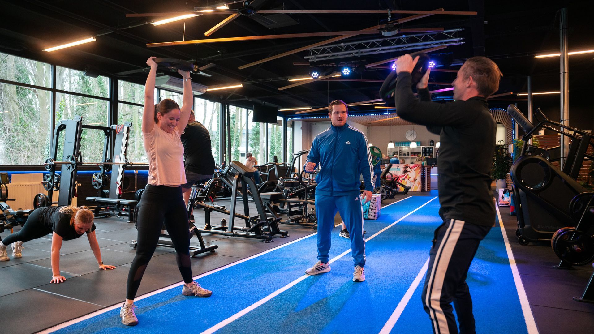 Mensen trainen in een sportschool. Een vrouw doet gewichtheffen boven het hoofd.