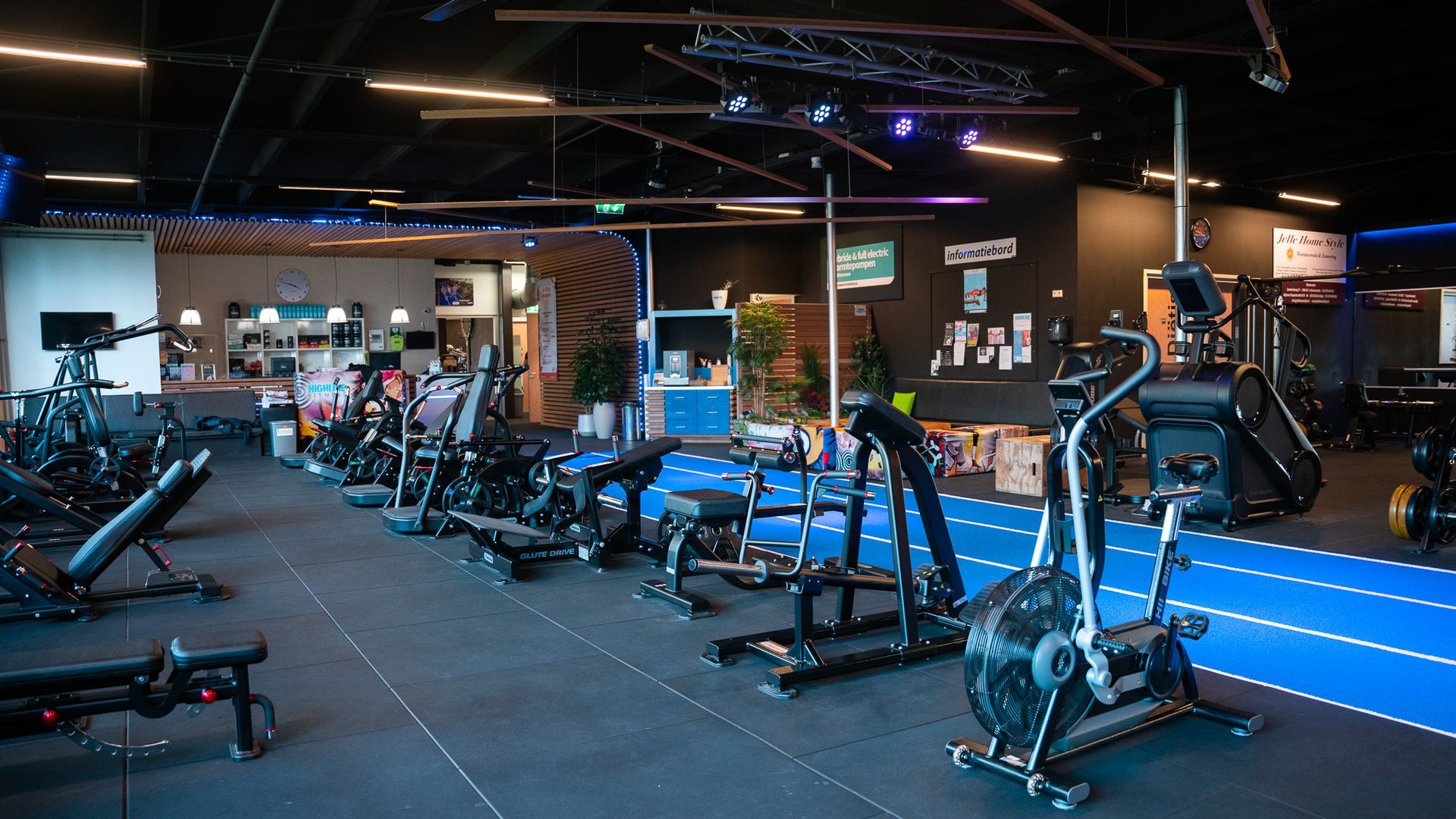 Interieur van een sportschool met fitnessapparaten op een zwarte vloer, een blauwe atletiekbaan.