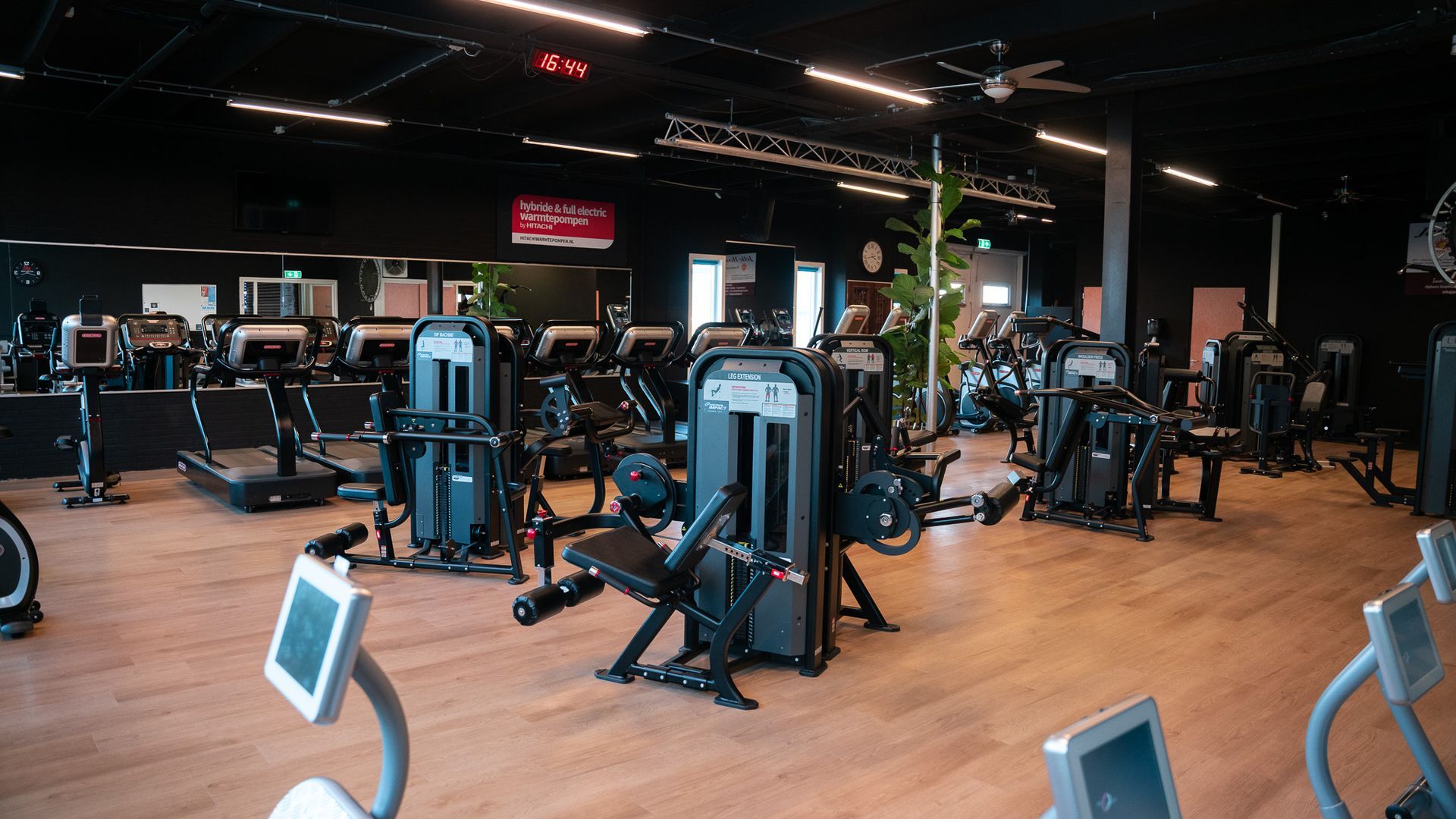 Interieur van een sportschool met verschillende fitnessapparaten, zwarte muren en bruine vloeren.