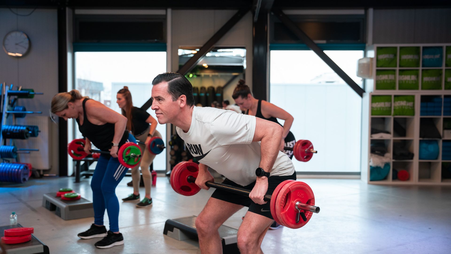 Mensen in de sportschool die halterrijen doen, onder begeleiding van een instructeur.