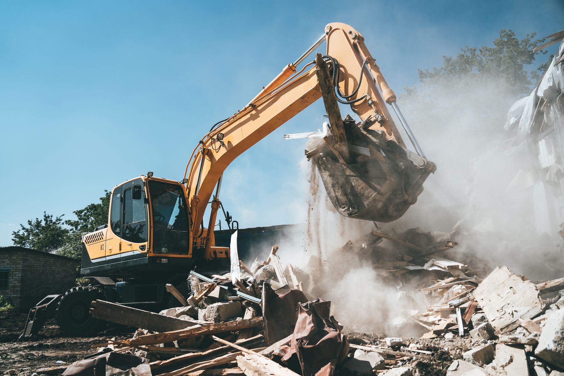 An excavator demolishing an old house, its bucket forcefully dismantles the concrete structure.