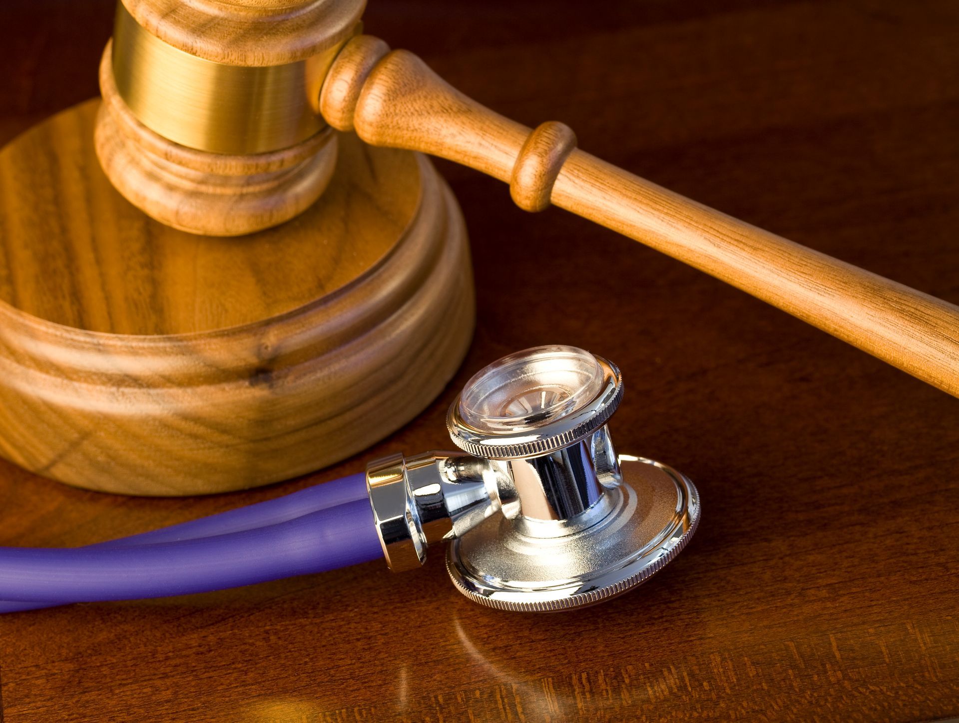 A stethoscope sits next to a wooden gavel on a wooden table
