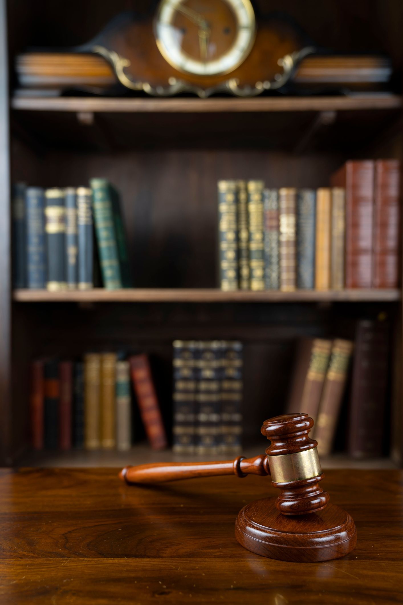 A wooden judge 's gavel is sitting on a wooden table in front of a bookshelf.