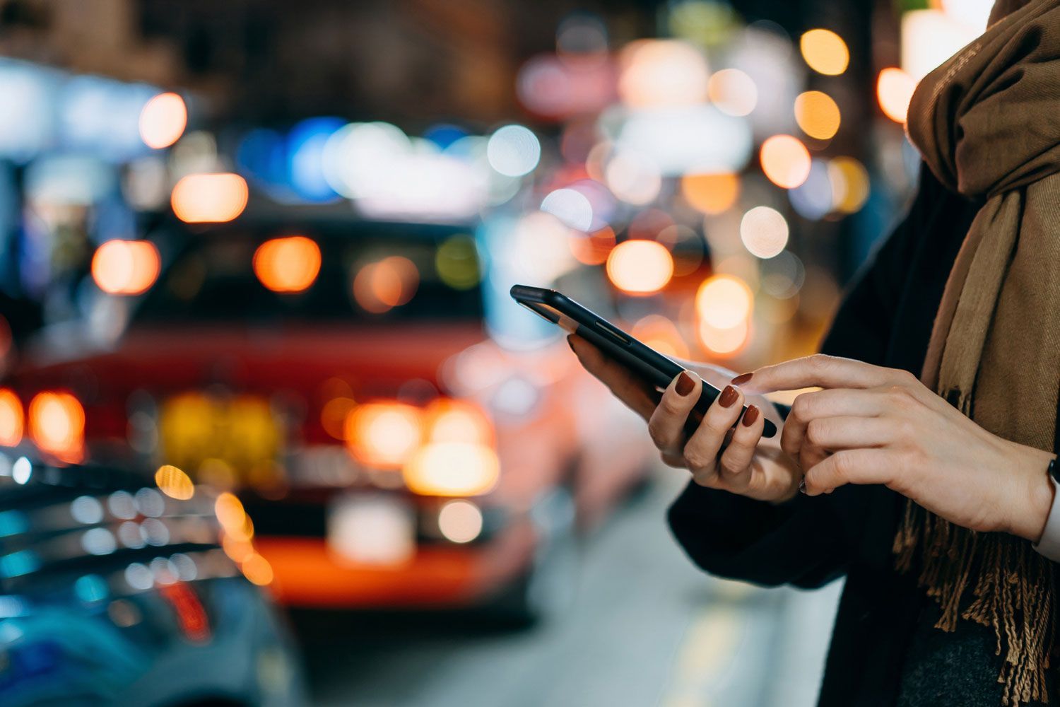 A woman is using a cell phone on a city street at night.