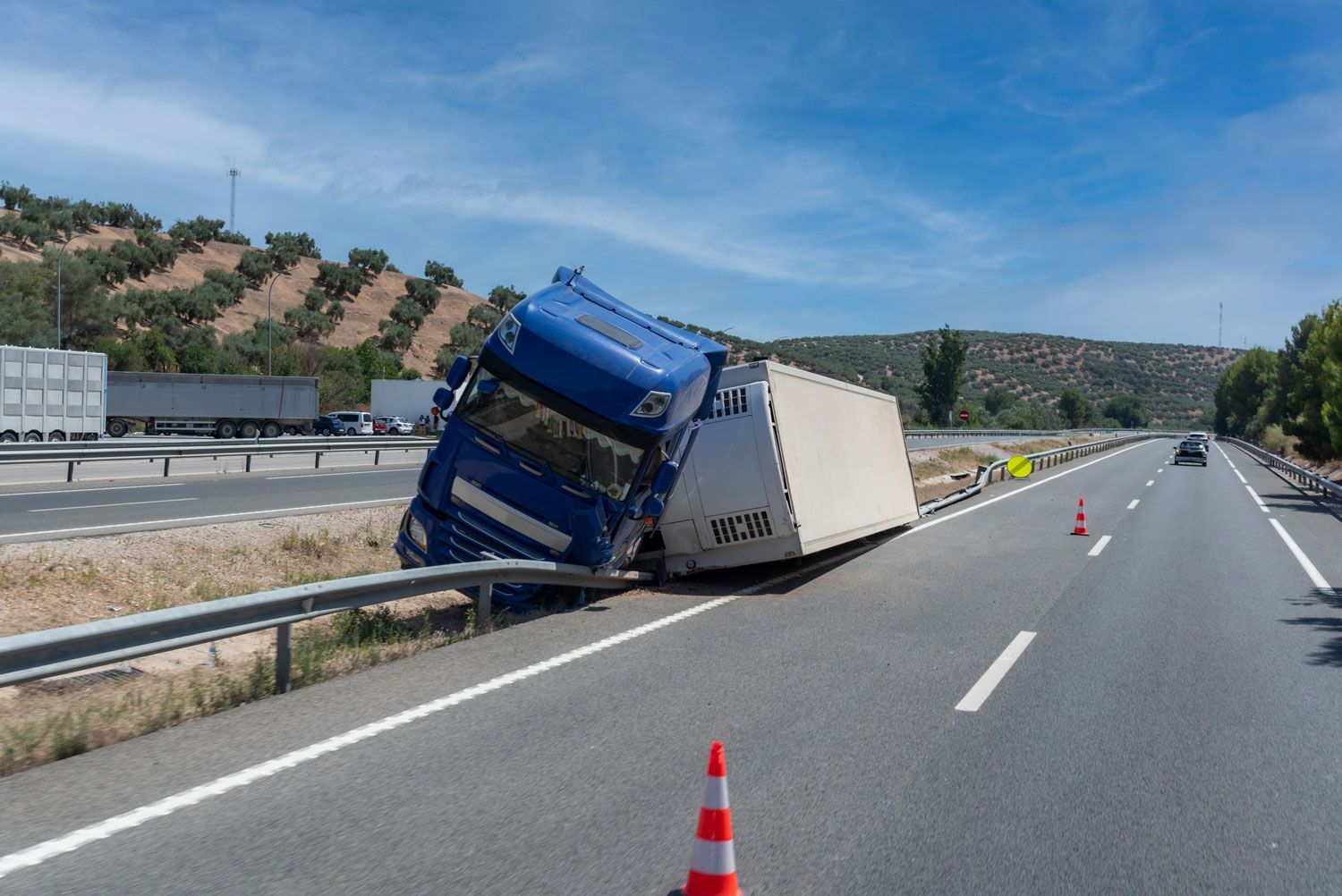 A blue semi truck is turned over on the side of a highway.