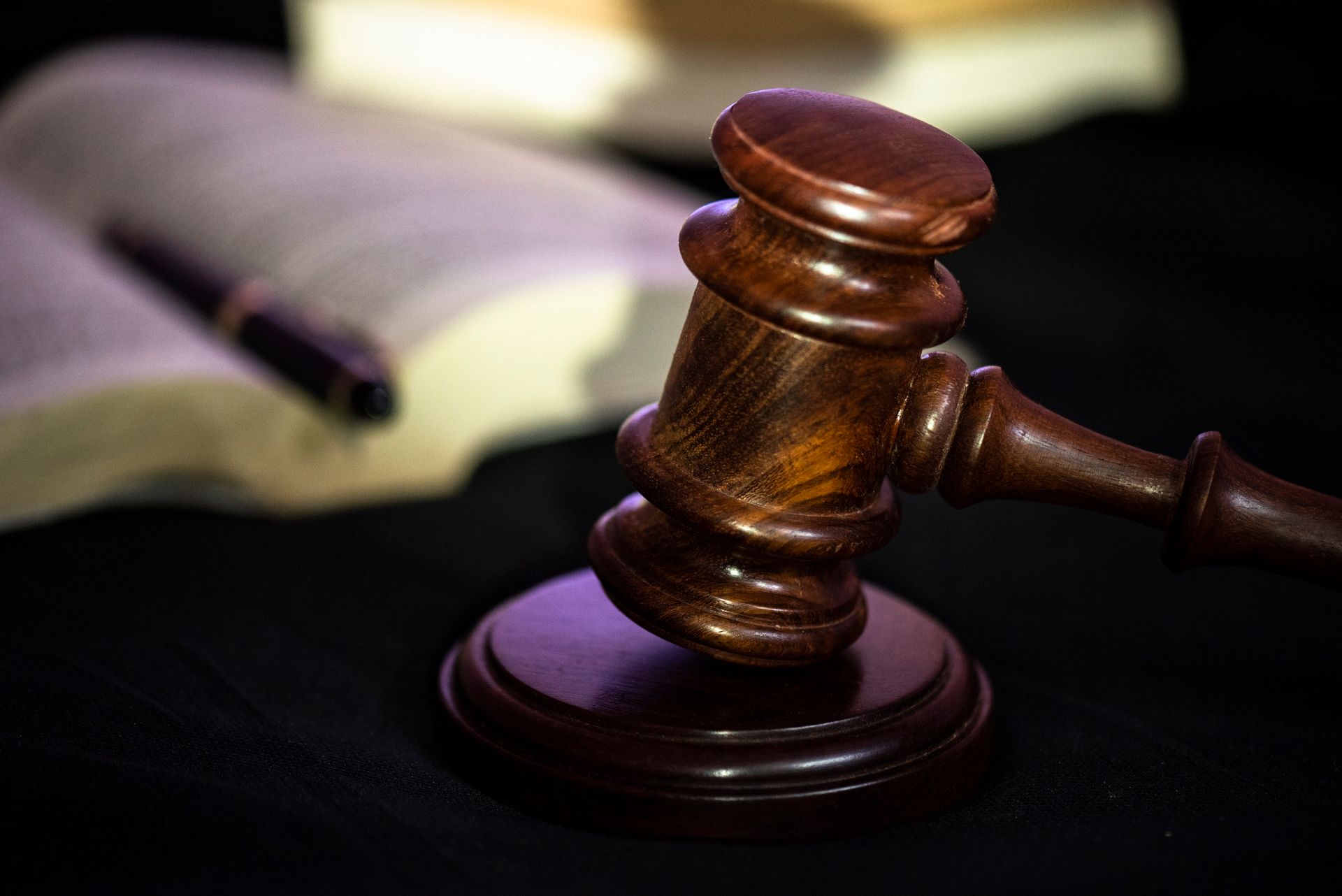 A wooden judge 's gavel is sitting on a table next to a book and a pen.