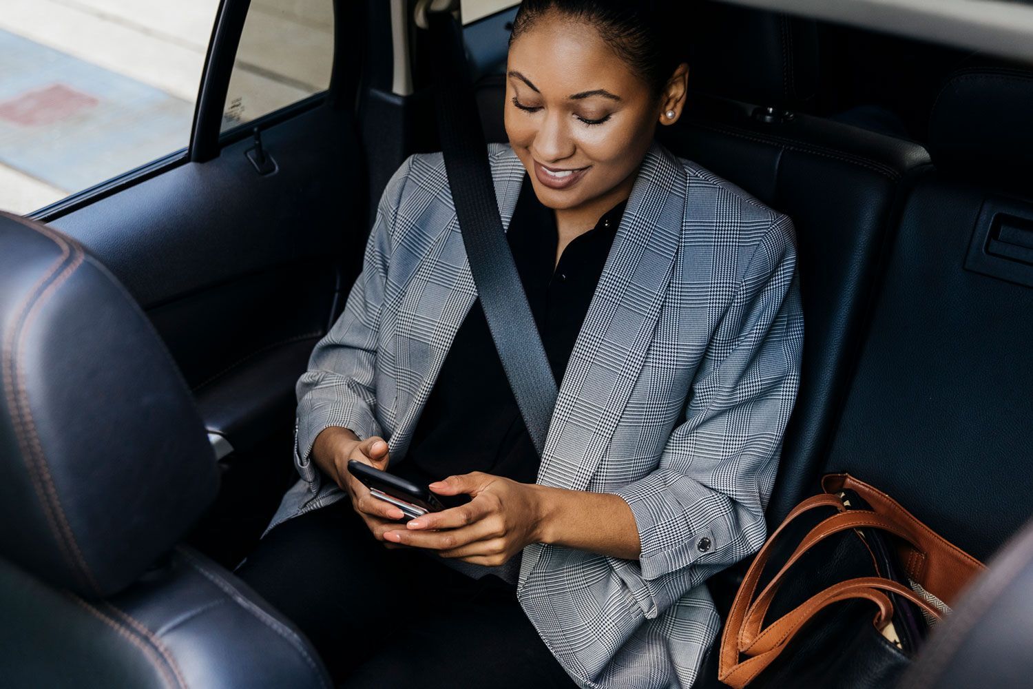 A woman is sitting in the back seat of a car looking at her cell phone.