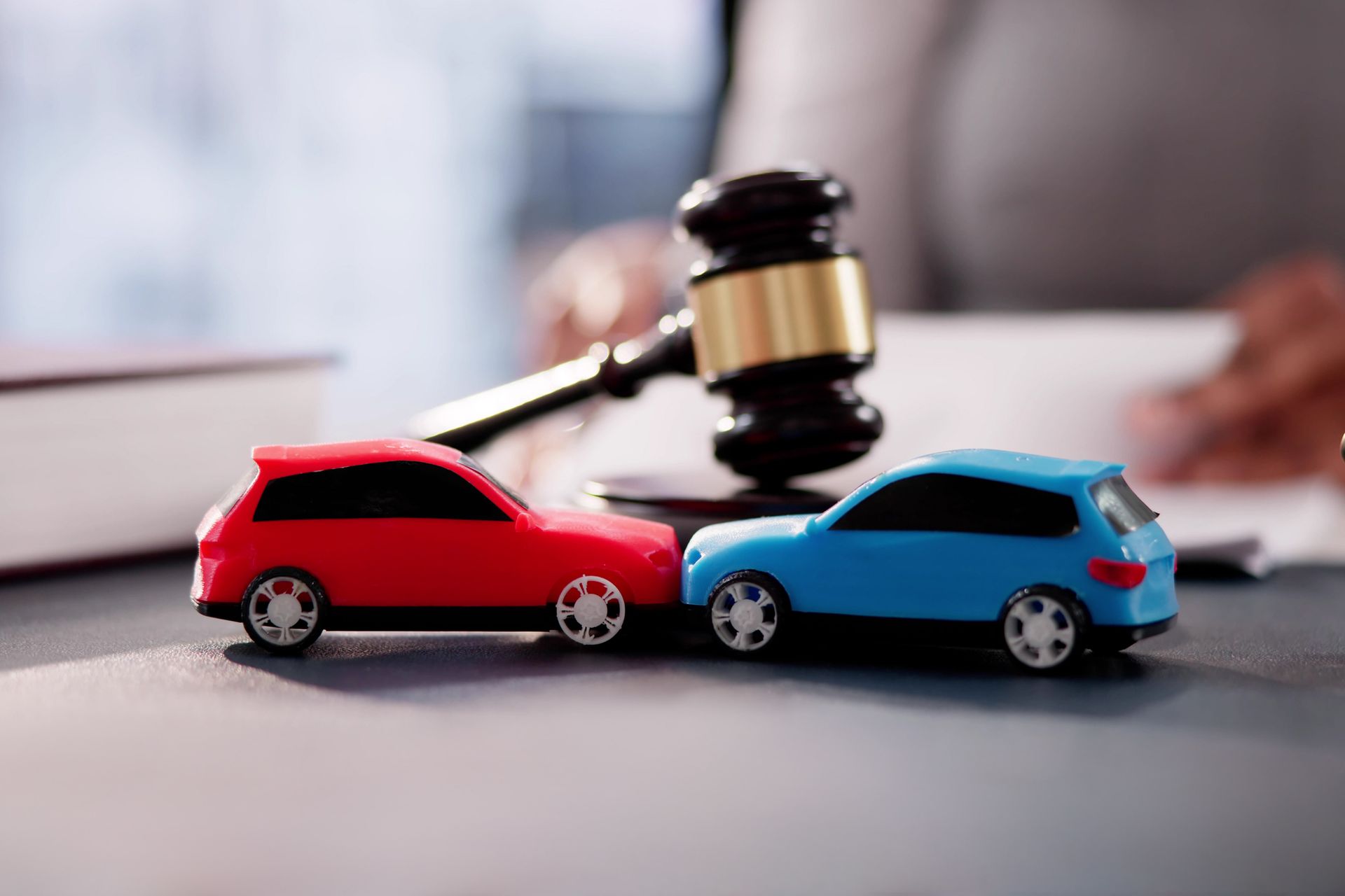 Two toy cars are sitting next to each other on a table next to a judge 's gavel. Two toy cars are sitting next to each other on a table next to a judge 's gavel.